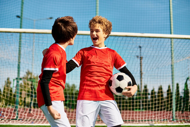 Δύο νεαροί με αθλητικά ρούχα στέκονται δίπλα-δίπλα σε γήπεδο ποδοσφαίρου, επιδεικνύοντας ομαδική δουλειά και συντροφικότητα.. - Φωτογραφία, εικόνα