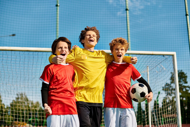 A group of young boys, all dressed in soccer jerseys, stand closely together in unity on a green soccer field. Each boy is looking in different directions, some talking and laughing, while others are focused and ready to play. - Photo, Image