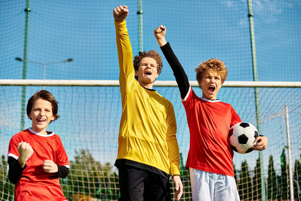 Egy csapat energikus fiatal fiú győzedelmesen áll a focipálya tetején, győzelmüket ünnepelve. A zöld fű és a mező fehér vonalai élénk hátteret teremtenek, ahogy a fiúk kötődnek a sport iránti közös szeretetükhöz.. - Fotó, kép