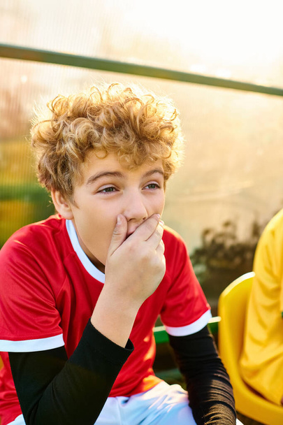 Ein kleiner Junge mit nachdenklichem Gesichtsausdruck sitzt auf einer Bank, die Hand sanft auf den Mund gelegt. - Foto, Bild
