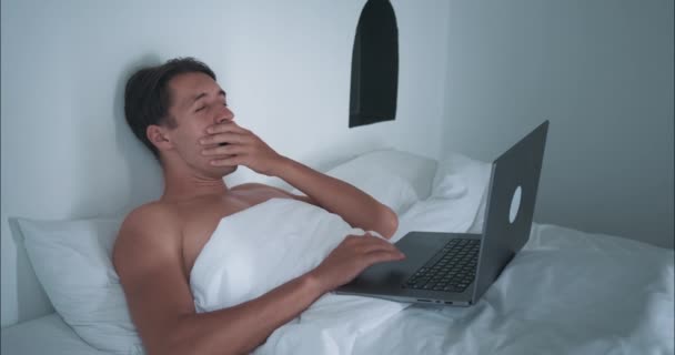 Muž ležící v posteli pracuje na notebooku a zavírání notebooku si dává pracovní pauzu. Pracovní přestávka v posteli symbolizuje moderní pracovní flexibilitu z domova Opření se oceňuje pracovní přestávka těší moment odpočinku - Záběry, video