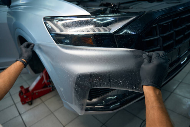 De mens brengt anti-grind film aan op het lichaam van een auto, de auto staat op een krik - Foto, afbeelding