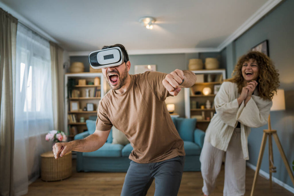 mężczyzna Dojrzałe dorosły biały mężczyzna mąż z jego żona lub dziewczyna para w domu cieszyć się wirtualną rzeczywistość VR zestaw słuchawkowy z google na głowie zabawy nowoczesne technologie wypoczynek koncepcja kopia przestrzeń - Zdjęcie, obraz