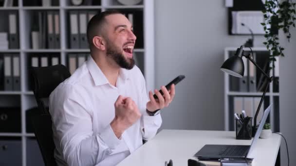 Удивительный, счастливый кавказский офисный работник разговаривает по телефону и празднует достижение или успешную сделку, работая в офисе. Положительный результат, финансовый рост. - Кадры, видео