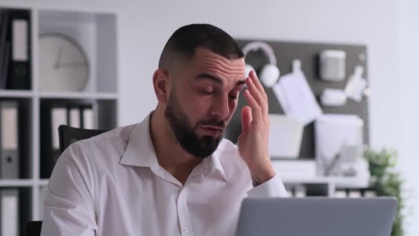 Portrét frustrovaného bělocha, který pracuje s laptopem a obličejem, sedí u stolu v kanceláři. Reakce na chybu nebo chybu, ohromen selháním. - Záběry, video
