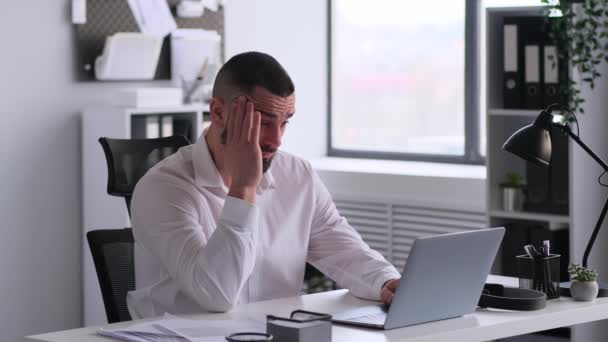 Masasında dizüstü bilgisayarla çalışan, ciddi bir beyaz erkek çalışanın baş ağrısı ya da migreni var. Yorgunluk, tükenme kavramı. - Video, Çekim