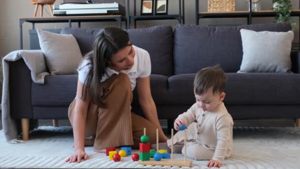 Дитячий хлопчик і щаслива мати грають з іграшками, займаються навчальним та ігровим процесом, проводять активне дозвілля, сидячи на підлозі в домашній вітальні. - Кадри, відео