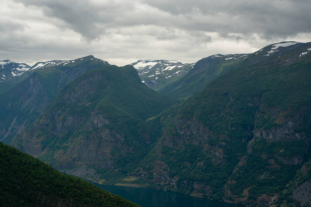 Nature view of Norwegian mountains with white snow cover on its high ground from stegastein viewpoint on a cloudy summer day. Blue uv radiation on the mountains. - Photo, Image