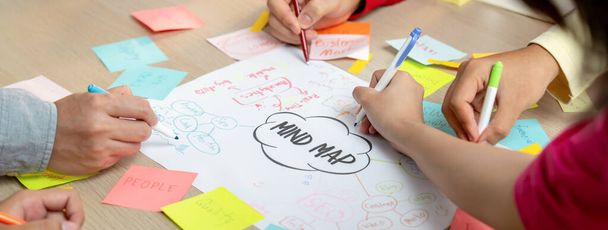 Professionelle Startup-Gruppe teilen kreative Marketing-Idee, indem sie Mindmap verwenden. Junge, qualifizierte Geschäftsleute erstellen Geschäftspläne, während sie klebrige Notizen schreiben. Konzentrieren Sie sich auf die Hand. Nahaufnahme. Bunt gemischt. - Foto, Bild