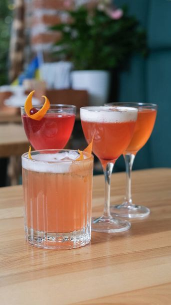 Τέσσερα αλκοολούχα κοκτέιλ σε ποτήρια σε ξύλινο τραπέζι καφετέριας. - Φωτογραφία, εικόνα