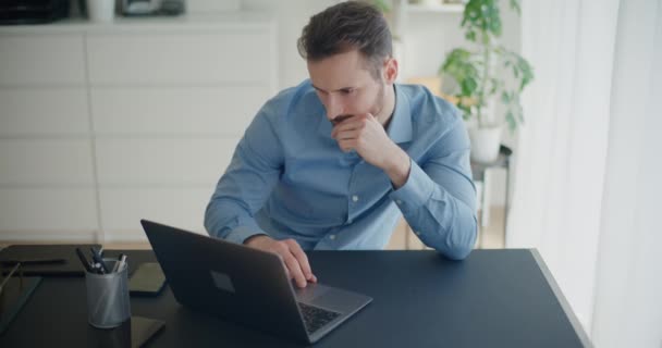 Empresario joven determinado que usa el ordenador portátil en el escritorio mientras trabaja en la oficina corporativa - Metraje, vídeo