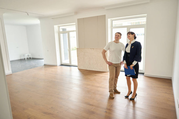 Женщина риэлтор знакомит клиента с новым домом, комната просторная и светлая - Фото, изображение
