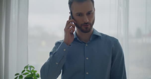 Kendine güvenen sakallı, genç ve yakışıklı işadamı çalışma alanının penceresinde beklerken telefonla stratejiyi tartışıyor. - Video, Çekim
