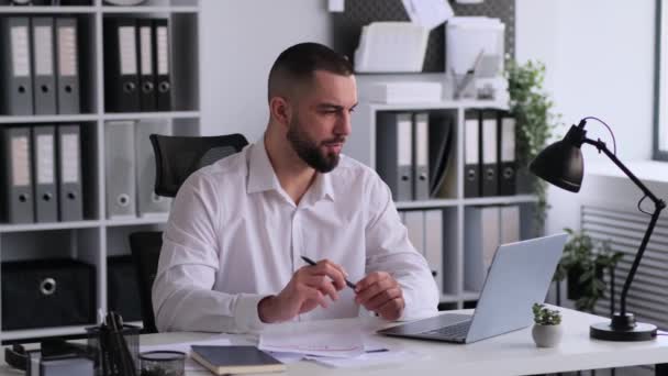 Pracovník nebo ředitel kavkazské kanceláře pracující a dirigující online konference s využitím notebooku v kanceláři, zabývající se papírováním a dálkovou komunikací. - Záběry, video
