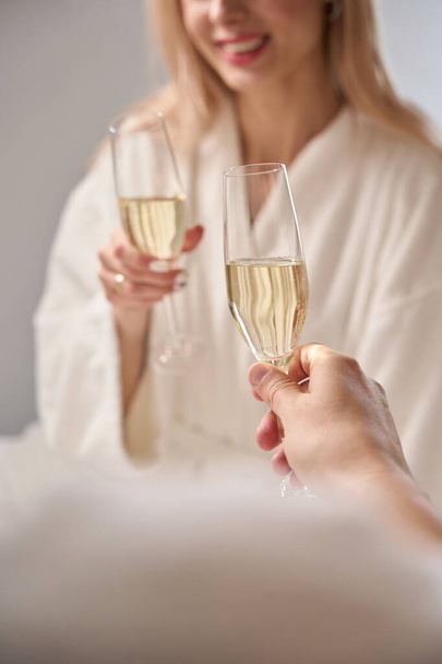 Romantik çift bir kadeh şampanya içerken kurnazca konuşuyor, kabarık bornozlu insanlar. - Fotoğraf, Görsel