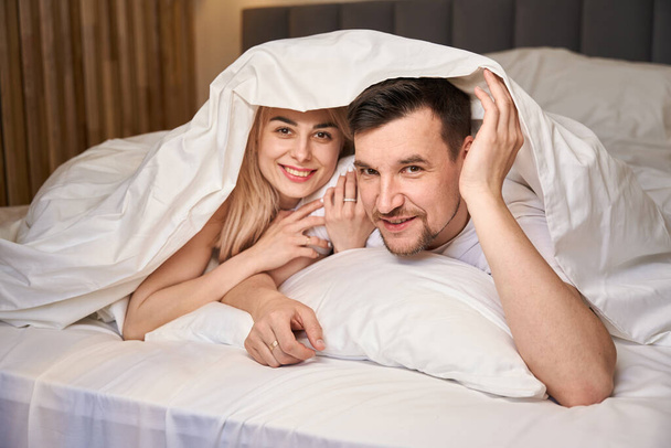 Jong stel is comfortabel gevestigd in een huwelijksreis kamer, ze liggen op een groot bed - Foto, afbeelding