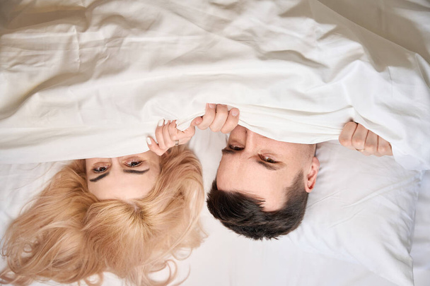 Gelukkig pasgetrouwden genesteld comfortabel onder een deken op een groot bed, paar in huwelijksreis kamer - Foto, afbeelding