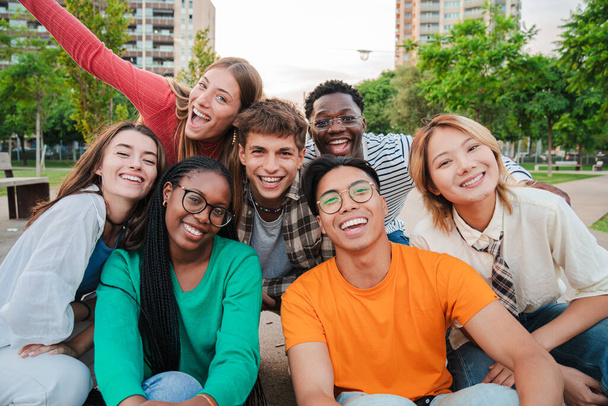 Big group of young adult real people smiling and having fun outdoors at vacations. Portrait of happy friends laughing. University teenage students on a social gathering. Multiracial teenagers meeting - Photo, Image