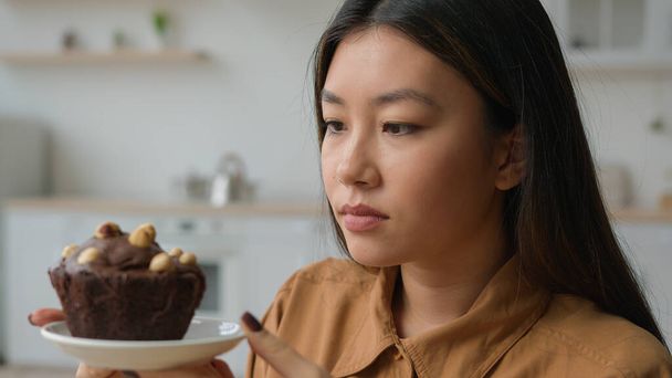 Asiatische koreanische Frau hungrig Mädchen in der Küche halten kalorienreiche Kuchen verweigern Schokolade Dessert essen halten Diät Gewicht verweigern Mehl Gluten süße Lebensmittel keine Zuckersucht aufhören Überessen vermeiden ungesunde Ernährung - Foto, Bild