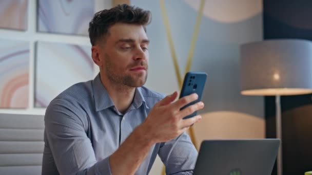 Relaxed man scrolling smartphone feed enjoying break at private cabinet closeup. Brunette smiling designer reading social media using mobile phone at office. Happy guy browsing internet alone indoors - Footage, Video