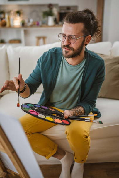 современный человек с бородой и усами живопись краски на дому держать кисть - Фото, изображение