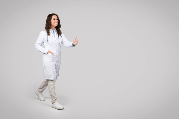 Positive european woman doctor with stethoscope, in uniform give hand to patient to handshake on light background, full length, free space. Medical services, professional health care - Photo, Image