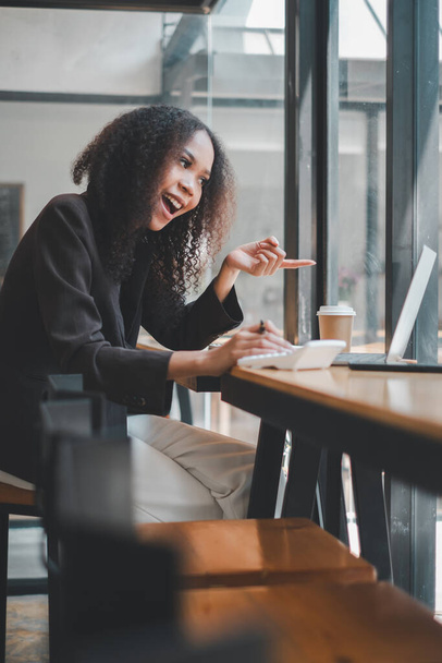 Μια εκφραστική επιχειρηματίας δείχνει την οθόνη του laptop της ενώ εργάζεται σε ένα καφέ, την αλληλεπίδρασή της προτείνοντας μια δυναμική διαδικασία εργασίας ή μια εικονική συνομιλία. - Φωτογραφία, εικόνα