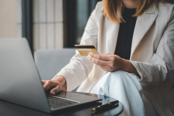 現代的な設定でプロの女性は自信を持って,現代の電子商取引とビジネスのシンボルであるクレジットカードとラップトップを使用してオンライン購入を行います. - 写真・画像