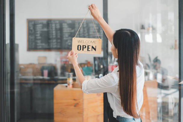 A dedicated cafe owner hangs an inviting 'Welcome Open sign, signaling the start of the day in her cozy coffee shop, an emblem of small business hospitality and readiness. - Photo, Image