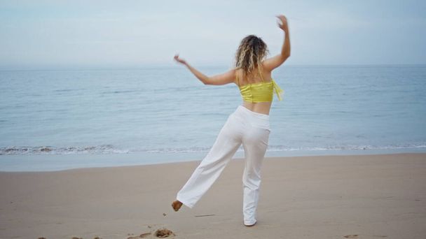 Energetic girl dancing beach looking on beautiful ocean waves. Back view curly woman dancer performing modern style improvisation on sea shore. Sensual young choreographer moving body in dance outdoor - Fotó, kép