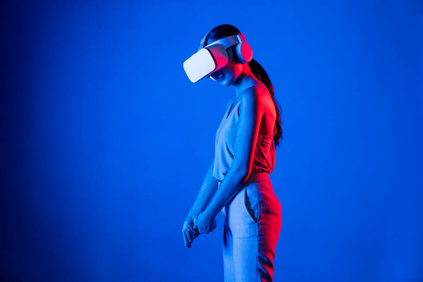 Inteligentna kobieta nosząca zestaw słuchawkowy VR łączący metawszechświatową, przyszłą technologię społeczności cyberprzestrzeni. Elegancka kobieta obliczająca i kontrolująca wirtualnego miotacza poważnie grającego w golfa. omamy. - Zdjęcie, obraz