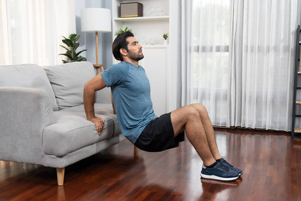 Corps athlétique et homme sportif actif utilisant des meubles pour cibler efficacement l'exercice de gain musculaire à la maison de gaieté comme concept de mode de vie sain d'entraînement à domicile du corps. - Photo, image