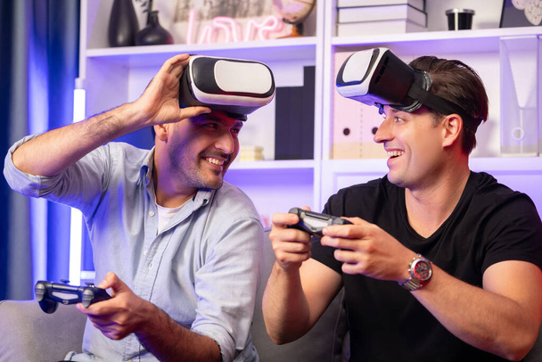 Buddy ystävä pelaajat pelaavat videopeliä joysticks ja VR kuulokkeet virtuaalisen teknologian todellisuudessa studiohuoneessa neon sininen valo. Mukava elää sisätiloissa iloinen taistelevat voittaja. Myytävissä. - Valokuva, kuva