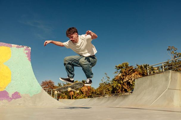 Aktive Skateboarder springen und einen Trick in einer Rampe eines Skateparks ausführen - Foto, Bild
