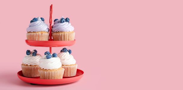 Lekkere cupcakes met bosbessen op standaard tegen roze achtergrond met ruimte voor tekst - Foto, afbeelding