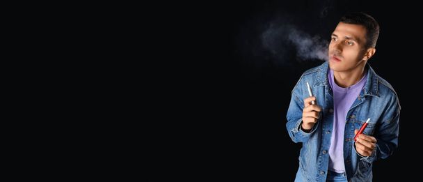 Νεαρός άνδρας καπνίζει ηλεκτρονικά τσιγάρα σε μαύρο φόντο με χώρο για κείμενο - Φωτογραφία, εικόνα