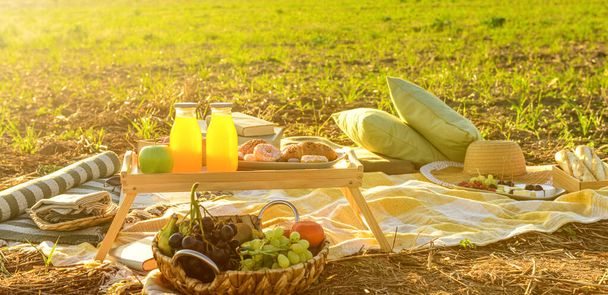 Plaid z butelkami soku i przekąski na piknik na polu o zachodzie słońca - Zdjęcie, obraz