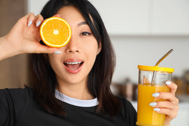 Sportos ázsiai nő narancssárga és üveg gyümölcslé a konyhában, közelkép - Fotó, kép