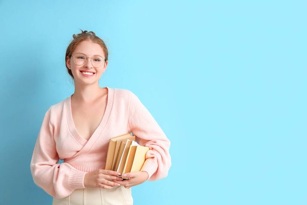 Young woman with stack of books on blue background - Foto, Imagen