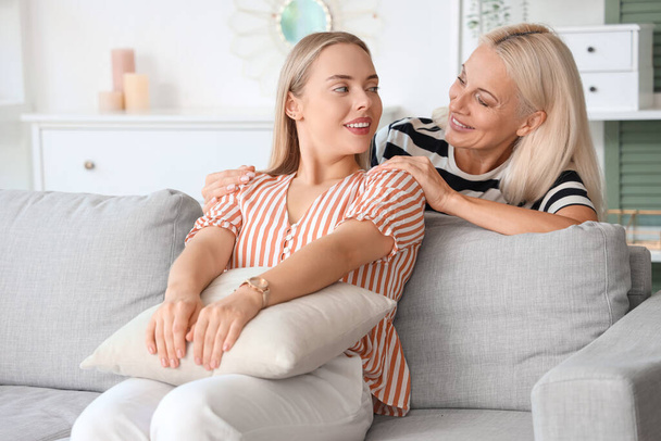 Happy young beautiful woman with her mother sitting on sofa in living room - Photo, Image
