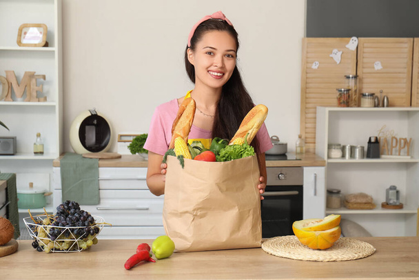 Beautiful young Asian woman with melon and bag full of fresh products in kitchen - Photo, Image