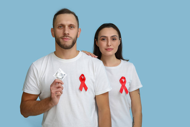 Young couple with red ribbons and condom on blue background. AID awareness concept - Photo, Image