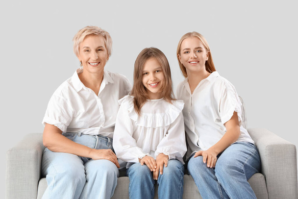 Little girl with her mom and grandmother sitting on sofa against light background - Photo, Image