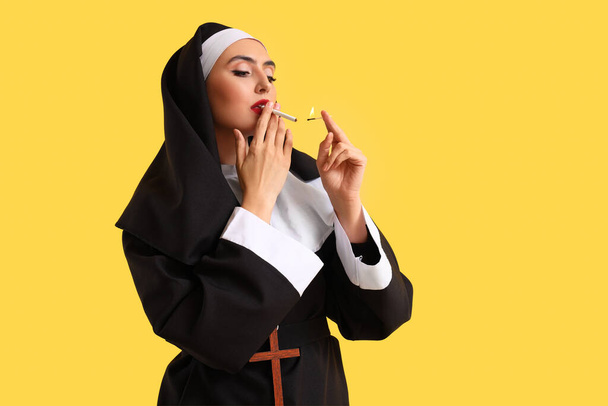 Naughty nun lighting cigarette on yellow background - Photo, Image