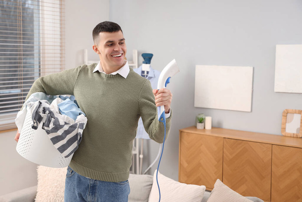 Szczęśliwy młody człowiek z parowcem i koszem pełnym prania w domu - Zdjęcie, obraz