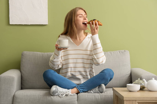 Nuori nainen kupin teetä syöminen croissant kotona - Valokuva, kuva