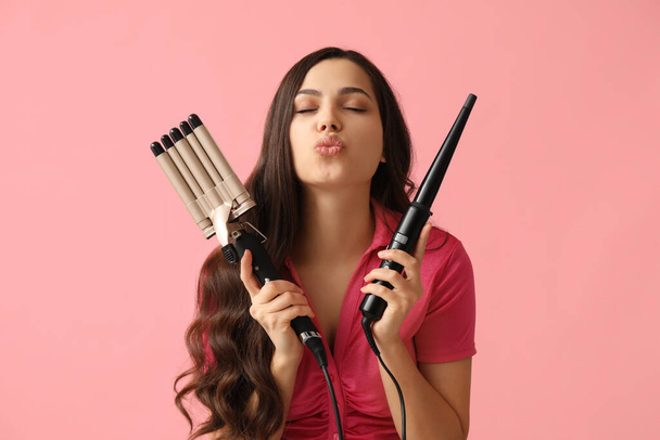 Beautiful young woman with different curling irons on pink background - Фото, изображение