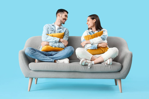 Beautiful young happy couple resting on sofa against blue background - Photo, Image