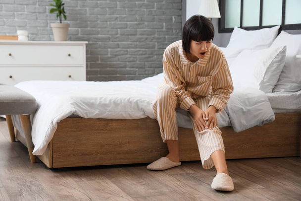Mujer joven que sufre de dolor de rodilla en el dormitorio - Foto, imagen
