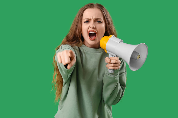 Giovane donna arrabbiata con megafono che punta lo spettatore su sfondo verde. Concetto di accusa - Foto, immagini